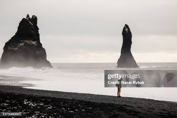 ein junger mann genießt im winter die aussicht am schwarzen sandstrand von reynisfjara - black sand iceland stock-fotos und bilder