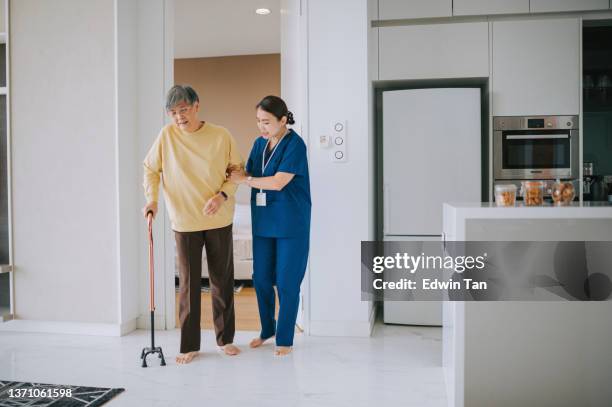 asian chinese female nurse helping senior woman practise walk with walking stick in living room. senior patient with walking frame and nurse - dementia 個照片及圖片檔