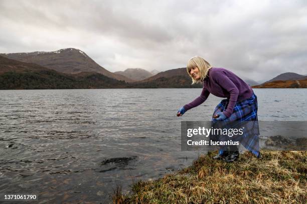 woman skimming flat stones in loch arkaig in the highlands of scotland - woman kilt stock pictures, royalty-free photos & images