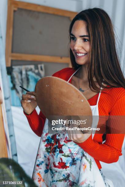 female painter drawing in art studio using easel. portrait of a young woman painting with aquarelle paints on white canvas - acrylic painting stock pictures, royalty-free photos & images