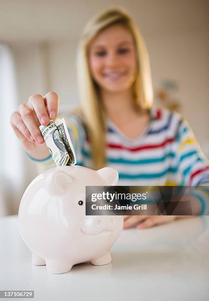 teen girl putting money into piggy bank - blonde girl piggy bank stock-fotos und bilder