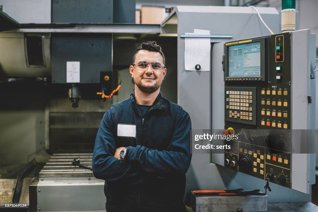 Retrato de engenheiro aprendiz sorridente trabalhando com máquina CNC na fábrica