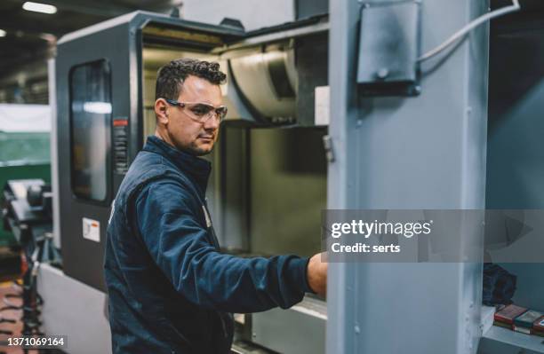 männlicher ingenieurlehrling, der mit cnc-maschine in der fabrik arbeitet - rechnerunterstützte fertigung stock-fotos und bilder