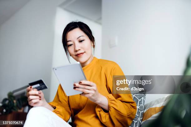 beautiful smiling young asian woman relaxing at home, shopping online with digital tablet and making payment online with credit card. lifestyle and technology. contactless payment. enjoyable and easy shopping experience - banking document stock-fotos und bilder