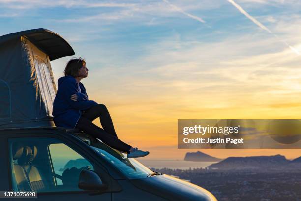 mature woman taking in the view at sunset from the roof of her campervan - road trip van stock pictures, royalty-free photos & images