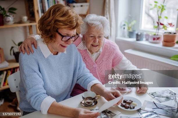 Senior mother with her adult daughter looking at old family pictures at home together.