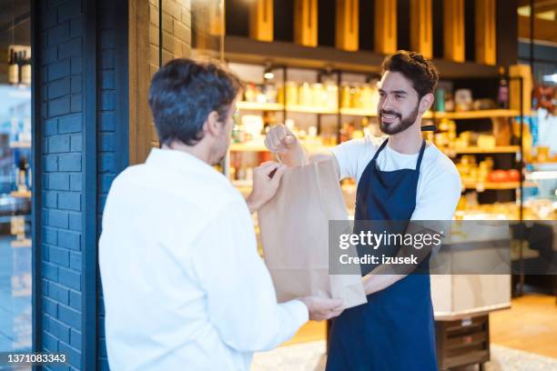 young salesman giving paper bag to customer - giving back bildbanksfoton och bilder