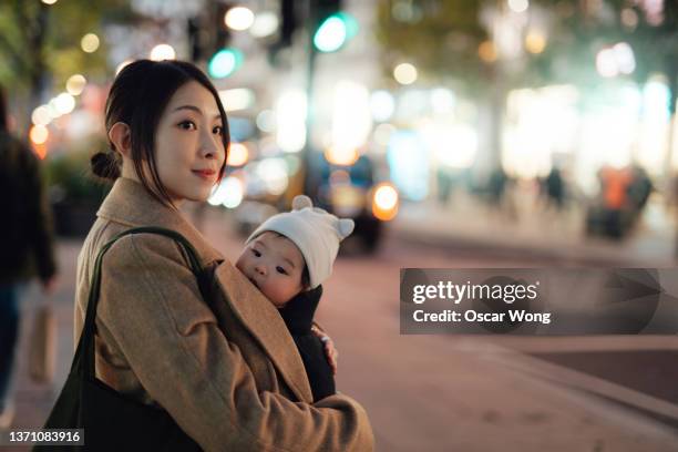 young asian mother with baby waiting for taxi on city street - baby carrier stock pictures, royalty-free photos & images