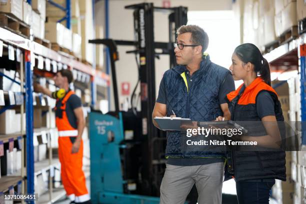 shop-floor operations in a warehouse management. warehouse foreman with checklist are discussing on delivery plan with asian female warehouse manager holding industrial tablet in a factory warehouse. - operations manager stock pictures, royalty-free photos & images