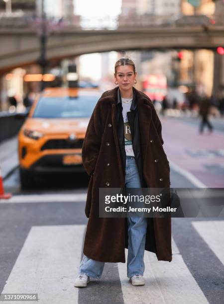 Millane Friesen is wearing a blue denim jeans, a grey hoodie and a brown long coat during New Yorker Fashion Week on February 15, 2022 in New York...