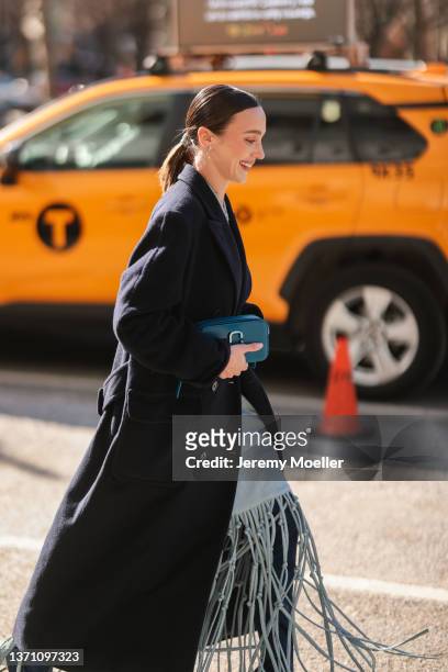 Mary Leest wears a pale grey halter neck / shoulder-off long dress, a black wool oversized winter coat, a navy blue shiny leather SnapShot handbag...