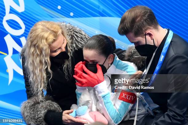 Kamila Valieva of Team ROC reacts as they wait for their score with choreographer Daniil Gleikhengauz and coach Eteri Tutberidze after the Women...