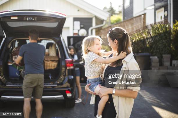 portrait of mother, father and two daughters standing by car at electric vehicle charging station - car in driveway foto e immagini stock