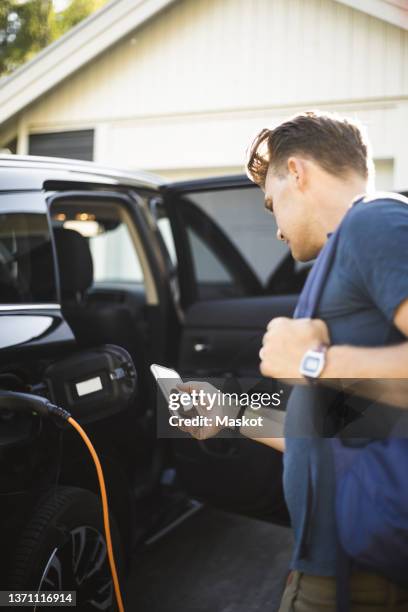 portrait of mother, father and two daughters standing by car at electric vehicle charging station - car on driveway bildbanksfoton och bilder