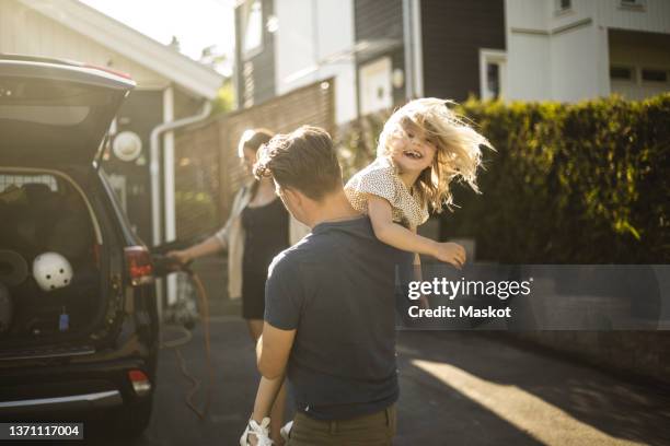 portrait of mother, father and two daughters standing by car at electric vehicle charging station - family holiday europe stockfoto's en -beelden
