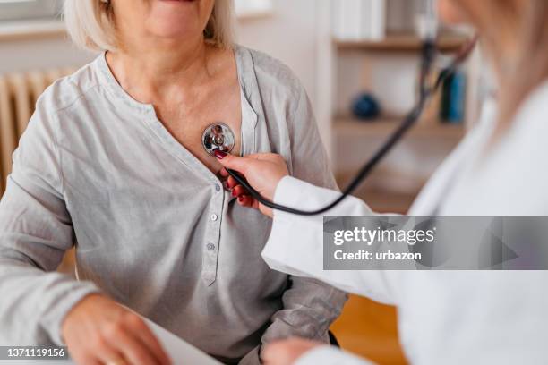 arzt, der einen älteren patienten auskultiert - stethoscope heart stock-fotos und bilder
