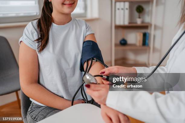 arzt misst blutdruck eines jungen patienten - bluthochdruck stock-fotos und bilder