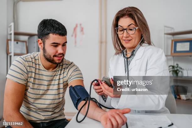 médico medindo pressão arterial de um jovem paciente - instrumento de medição - fotografias e filmes do acervo