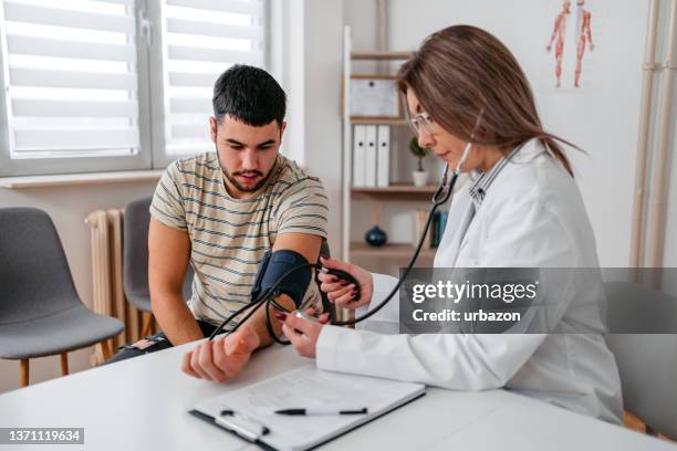 doctor measuring blood pressure of a young patient - measuring stockfoto's en -beelden