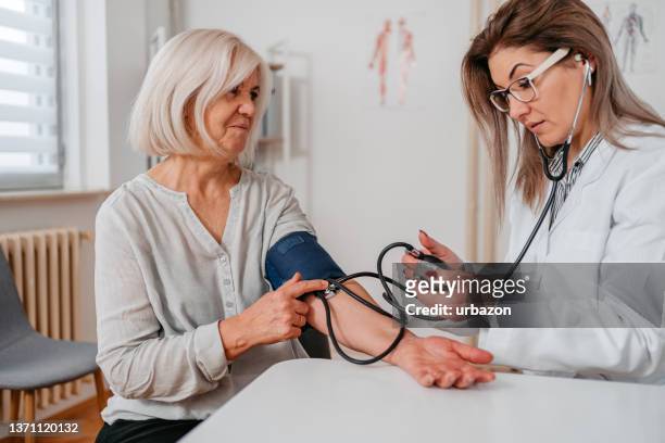 médico medindo pressão arterial de um paciente sênior - gauge - fotografias e filmes do acervo