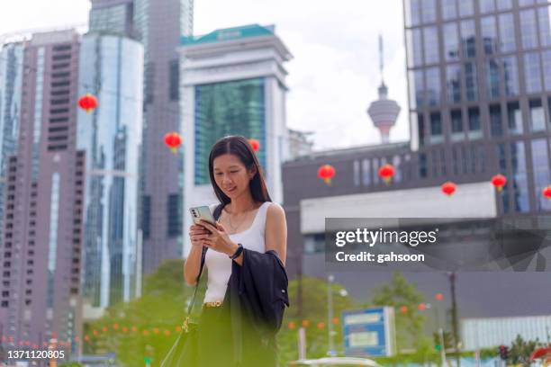 woman reading mobile phone on street with urban skyline - menara tower stock pictures, royalty-free photos & images