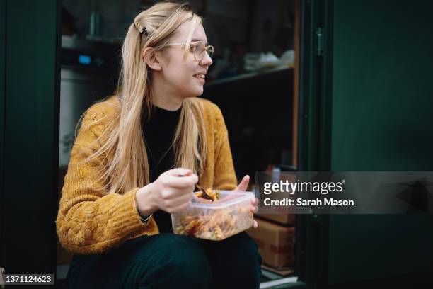 young woman sat on step eating lunch - bandeja fotografías e imágenes de stock