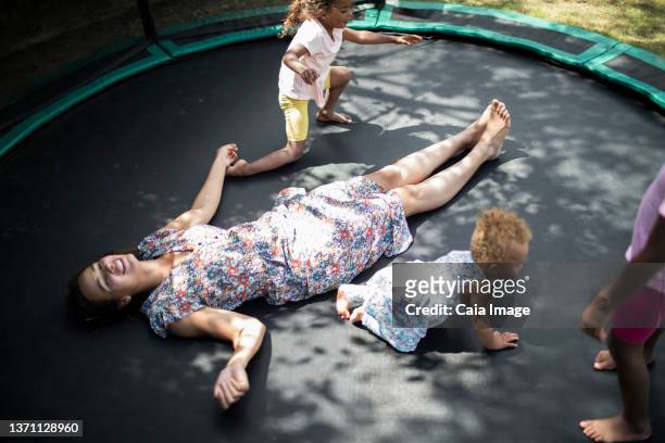daughters playing around carefree mother laying on trampoline - child lying down stock pictures, royalty-free photos & images