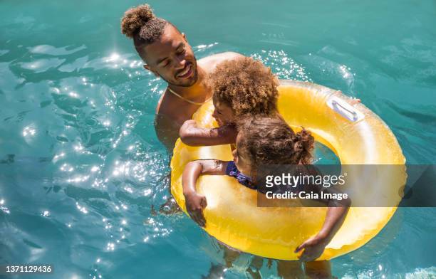 father and daughters in inflatable ring in sunny summer swimming pool - caiaimage stock-fotos und bilder