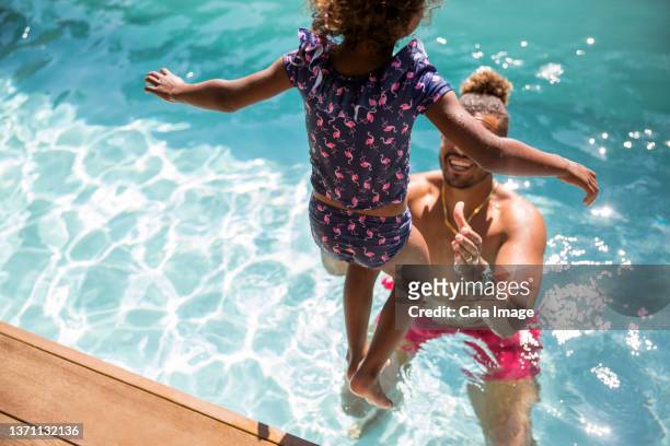 daughter jumping into arms of father in sunny swimming pool - jump dad stockfoto's en -beelden