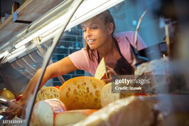 vendedora arreglando queso en vitrina - deli fotografías e imágenes de stock