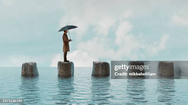 man walks on rocks in the water while holding umbrella - climate stock pictures, royalty-free photos & images