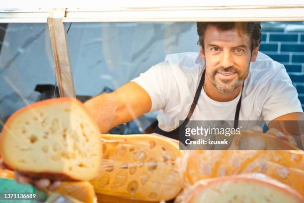 male owner removing fresh cheese from cabinet - cheesy salesman stockfoto's en -beelden