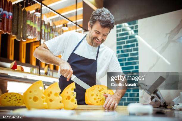 カウンターでチーズをカット笑顔の男性の所有者 - デリカッセン ストックフォトと画像