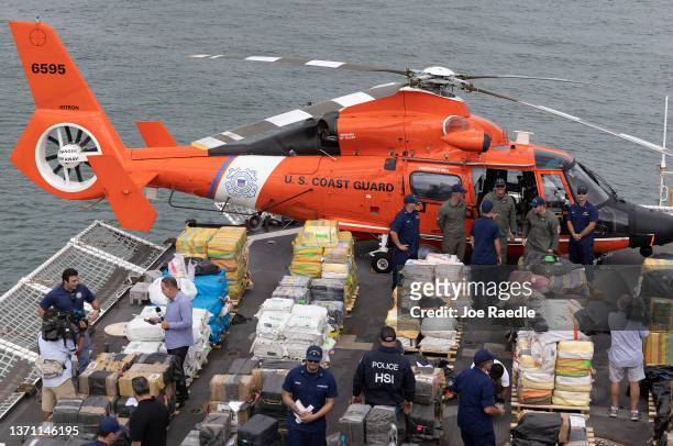 Coast Guard personnel and members of the media walk among wrapped packages of cocaine and marijuana on the deck of the Cutter James before offloading...