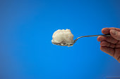 Pig fat or lard on a metal spoon held by Caucasian male hand. Close up studio shot, isolated on blue background