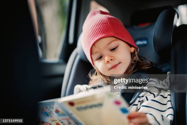 süßes kleines mädchen, das buch liest, während es mit dem auto reist - kid car seat stock-fotos und bilder