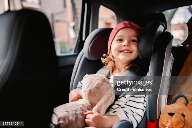 ritratto di una bambina che tiene in mano il suo giocattolo preferito mentre viaggia in auto - child car seat foto e immagini stock