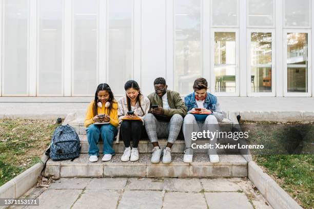 young multiracial students using cell phone sitting at campus school - mobile phones group stockfoto's en -beelden