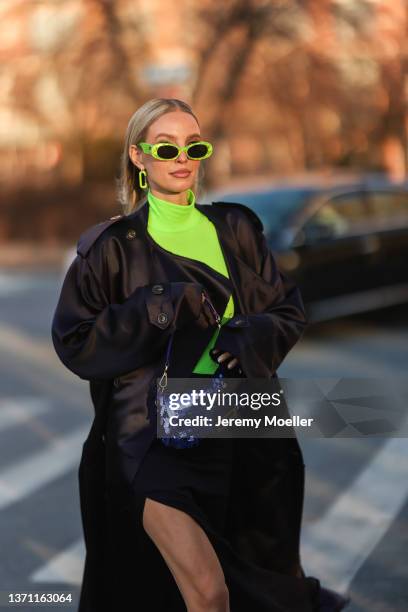 Leonie Hanne wears neon yellow earrings, a neon yellow turtleneck pullover, a black oversized rain long coat, black shorts with a long train, a navy...