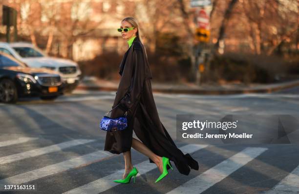 Leonie Hanne wears neon yellow earrings, a neon yellow turtleneck pullover, a black oversized rain long coat, black shorts with a long train, a navy...