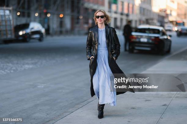 Lisa Aiken wears black sunglasses from Ray Ban, a gold large pendant necklace, a baby blue pleated / belted midi dress, a black shiny leather...