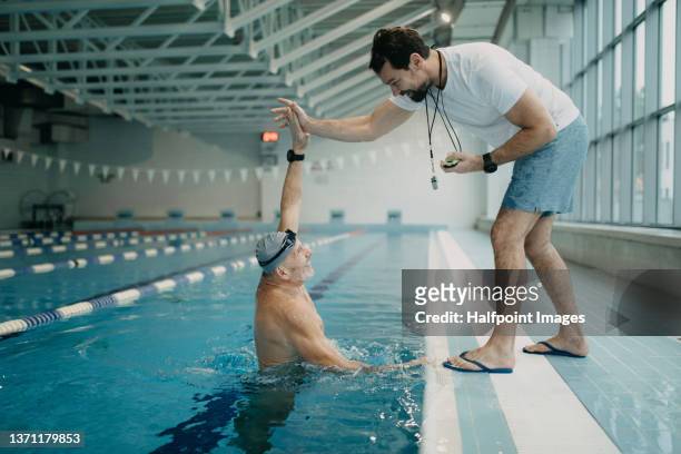 personal coach encouraging swimmer when swimming indoors in swimming pool. - allenatore foto e immagini stock