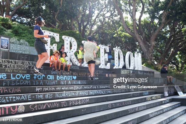 Family with young children sits near the large 'Freedom' lightbox sign erected by protestors on the steps leading to the Beehive on February 18, 2022...