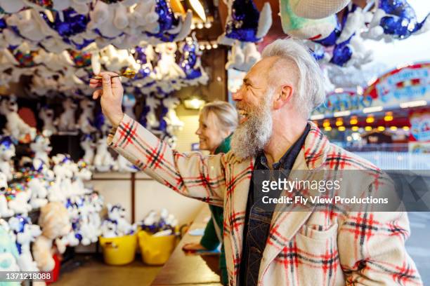 älterer mann mit spaß beim dartspielen auf dem karneval - carnival game stock-fotos und bilder