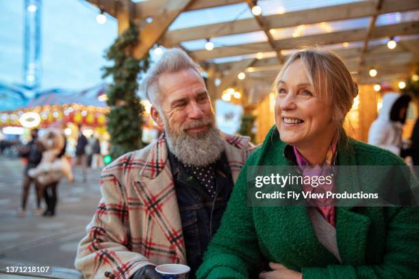 carefree senior couple eating at christmas market - mature couple winter outdoors stockfoto's en -beelden