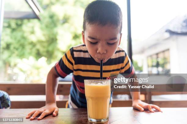 boy drinking juice with reusable silicone drinking straw - mango juice stockfoto's en -beelden