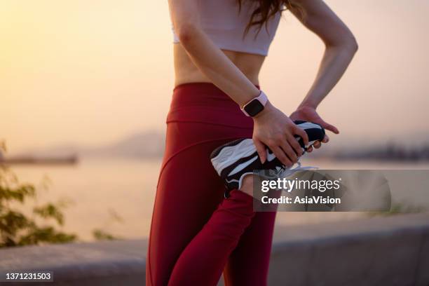 cropped shot of young asian sports woman in sportswear, stretching legs outdoors, standing by the promenade at sunset. getting ready to exercise. girl power. health and fitness concept - forward athlete stockfoto's en -beelden