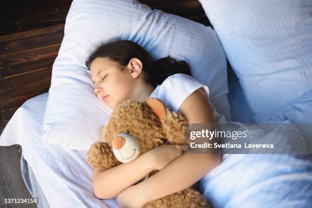 portrait of little sweet girl sleeping peacefully in a bed with her teddy bear. - child holding toy dog stock pictures, royalty-free photos & images