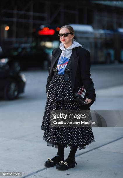 Chloe King wears black sunglasses from Saint Laurent, a gray with blue and red Nasa print pattern hoodie sweater, gold earrings, a black oversized...