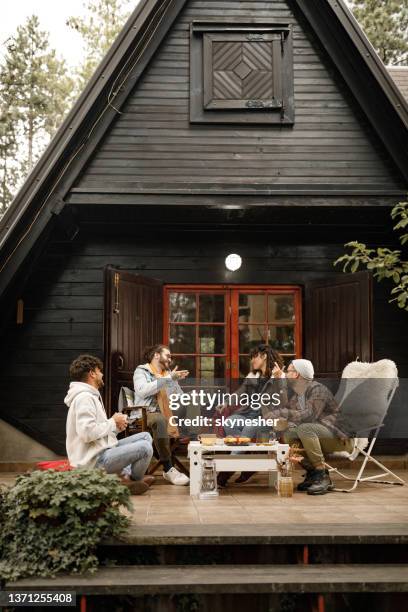 junge glückliche freunde, die sich auf einer terrasse vor der hütte unterhalten. - landhaus stock-fotos und bilder